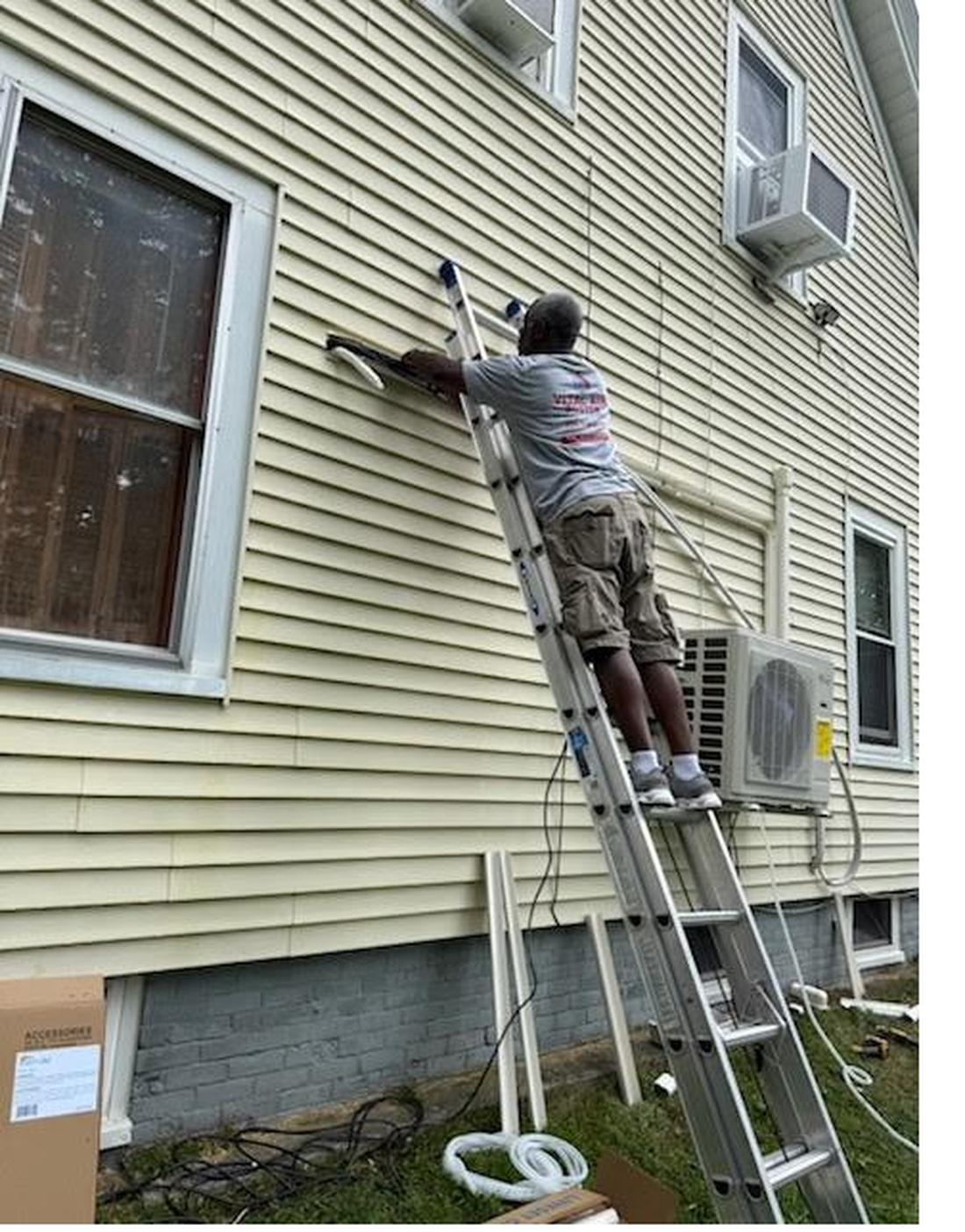 Hans installing a mini split condenser from a ladder